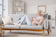 © Pixel-Shot - Young woman with short hair in headphones using mobile phone on sofa at home