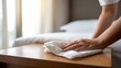 © Iuliia - Woman wiping dust on wooden table with white cloth. Female housekeeper cleaning furniture in hotel room. Hygiene concept for home and service industry.