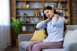 © Liubomir - Young indian woman sitting on sofa massaging neck and shoulders, showing cervical ache and muscle tension from poor posture, stress and fatigue at home