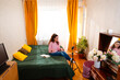 © _KUBE_ - Enthusiastic woman filming herself at home, sitting on a bed and sharing business insights. Wide shot
