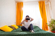 © _KUBE_ - Caucasian woman sitting on bed testing advanced VR technology for digital experiences, Concept of modern AI technology. Wide shot