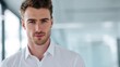 © Tanu - Young man stands in modern office space during daytime looking directly at the camera with a slight smile on his face and a confident expression
