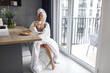 © Vlad - Pretty young woman sitting on the kitchen while drinking coffee. Woman with white towel on the head. Lifestyle concept