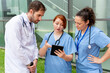 © StockMe - Medical team collaborating outdoors, using a digital tablet for healthcare data analysis and patient discussion