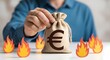 © sultan - Economic Inflation Crisis: Man holding burlap money bag with Euro symbol surrounded by paper fire, rising living costs, financial loss, energy prices and currency devaluation concept