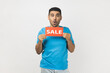 © khosrork - Portrait of shocked surprised unshaven man wearing blue T- shirt standing holding sale card in hands looking at camera with big eyes, black friday. Indoor studio shot isolated on gray background.