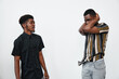 © SHOTPRIME STUDIO - Two young black men with dark skin in casual clothes having a tense conversation in studio. One man in black shirt looks serious, other in striped shirt covers face with arms.