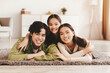 © Prostock-studio - Family portrait of happy asian millennial male, female and teen girl hugging, resting on floor with positive facial expression in living room interior. Family enjoy weekend at home, fun together