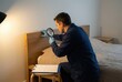 © Stitch - A pest control exterminator inspects a wooden headboard for bed bugs with a magnifying glass.