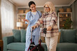 © Stockphotodirectors - A home health nurse helps an elderly woman with a walker in a living room. The two are talking as the nurse offers support during an afternoon home care visit.