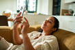 © Marko Geber - Young woman relaxing on sofa at home using smartphone