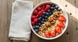© AgungPuja - A vibrant bowl of oatmeal topped with fresh raspberries, blueberries, sliced strawberries, walnuts, and almonds, served on a wooden table with a white napkin.