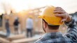 © JuliaDorian - Construction worker wearing yellow hard hat observes team building wooden structure at sunset, showcasing teamwork and dedication in construction industry