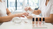 © Николай Чайка - Female nail technician applies nail polish to client's hand at a modern salon with various nail polish bottles and bowls of water on the table
