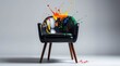 © kawan - A sleek, modern black armchair stands against a clean, light grey background, serving as a dynamic canvas for an explosion of vibrant, multi-colored paint. Bold splashes of red, orange, yellow, green,