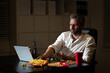 © Volodymyr - Business man eat pizza during a late night at office. An overworked man works on his laptop while having dinner in the workplace. Middle aged man eat takeaway meal while finishing office work at night