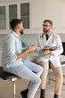 © fizkes - Medical anamnesis recording. Focused attentive doctor therapist hold clipboard pen listen to young male patient sharing complaints describing disease symptoms ask questions take notes in paper chart