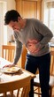 © Flash memory - Man experiencing stomach pain after eating breakfast in a domestic kitchen. Medical illustration of upset stomach, indigestion, heartburn concept.