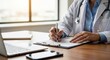 © ANDREY PROFOTO - Doctor writing medical report on clipboard at desk with laptop
