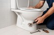 © whitestorm - A plumber fixing a toilet with an adjustable wrench and a screwdriver on a tiled floor, ensuring efficient plumbing maintenance and addressing common household issues.