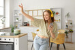 © Pixel-Shot - Cool young woman with mobile phone listening to music and dancing in kitchen