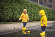 © Leka - Happy children playing with a paper boat in a puddle on a rainy day, joyful children in bright yellow raincoats and rubber waterproof boots - lifestyle