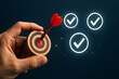 © PixelMasters - Hand holding target with red dart bullseye and glowing checkmarks on dark blue background - goal achievement, success, business objective and task completion concept
