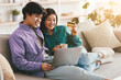 © Prostock-studio - Happy Asian couple shopping online via laptop and credit card, ordering things in internet, sitting on sofa at home, copy space. Happy customers, shopaholism and e-commerce concept