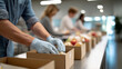 © perfectlab - Volunteers packing food items into cardboard boxes in a bright, organized community center or food bank setting with focus on gloved hands