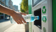 © miss irine - Person inserts plastic bottle into street recycling machine. Hand with bottle near slot. Green recycling symbols visible on machine. Urban environment, sunny day.