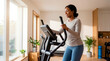 © Xenia - Black woman exercising on an elliptical machine at home. Smiling female working out in a bright living room. Healthy lifestyle and fitness concept