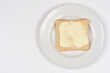 © nahhan - A single slice of crispy golden brown bread topped with a layer of creamy yellow butter served on a white ceramic plate against a plain white background