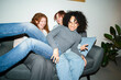 © Studio Marmellata - Three young women are laughing and enjoying time together on a sofa, sharing a moment of joy and connection.