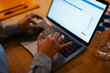 © Studio Marmellata - A person's hands are typing on a laptop keyboard, with a glass of water and a notebook on a wooden desk.