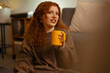 © Studio Marmellata - A young woman with curly red hair holds a yellow mug while sitting comfortably indoors, enjoying a warm beverage.