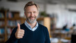 © Maksym - Professional education director smiling confidently and giving a thumbs-up gesture in a school classroom, soft depth of field, books and classroom elements subtly visible, neutral