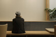 © Chutimon - Back view of a person sitting alone on a wooden bench against a minimalist wall