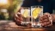 © CreativeArt - Older people hands holding refreshing sparkling water with lemon slice on a wooden table outdoors during summer