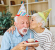 © Lumos sp - Senior couple celebreting birthday blowing cake candle and blowing a horn decoration making noise having fun