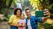 © ArtFocus Studio - Happy family taking a selfie with a smartphone in front of a beautiful waterfall in a lush green forest.