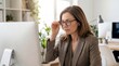 © YOUSSEF - Professional businesswoman adjusting glasses while focusing on computer work in bright modern office. Mature female executive concentration productivity workspace eyewear
