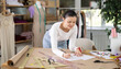 © JackF - Creative female seamstress designer drawing sketches on paper while sewing dress at workplace in small fashion sewing workshop