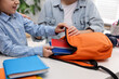 © New Africa - Mother and daughter packing backpack for school at desk indoors, closeup