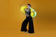 © New Africa - Beautiful young woman with piercings in fur coat and wide pants posing in color light on orange background
