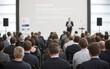 © KEYA - Audience engaged in a professional conference with a speaker presenting on stage