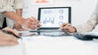 © NAMPIX - Business team discussing financial charts and data on a laptop during a meeting in a bright office.
