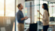 © al-sultan - Two individuals appear to be engaged in a conversation within a modern office setting. The image is blurred, emphasizing their interaction more than specific details.