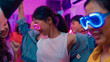 © tirachard - Closeup group multiethnic young adult Asia friend wear futuristic neon glowing glasses dance and drink alcohol beer fun hangout party in living room night indoor home. Disco lights illuminating house.