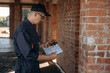 © standret - Documents and leveler tool are in hands. Builder is working on construction site, unfinished building