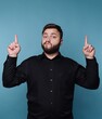 © bodnarphoto - Confident man posing against a blue background, playfully pointing upward with a charming expression